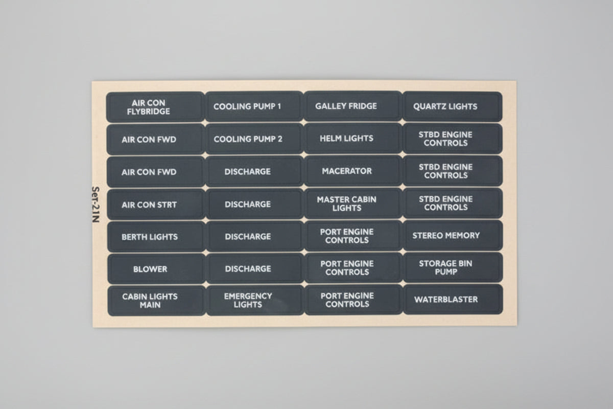 A dark gray rectangular panel filled with small light-blue and white rectangular labels arranged in a grid, showing automotive or technical system names such as air con, cooling pump, galley fridge, quartz lights, master cabin, engine controls, and waterheater.