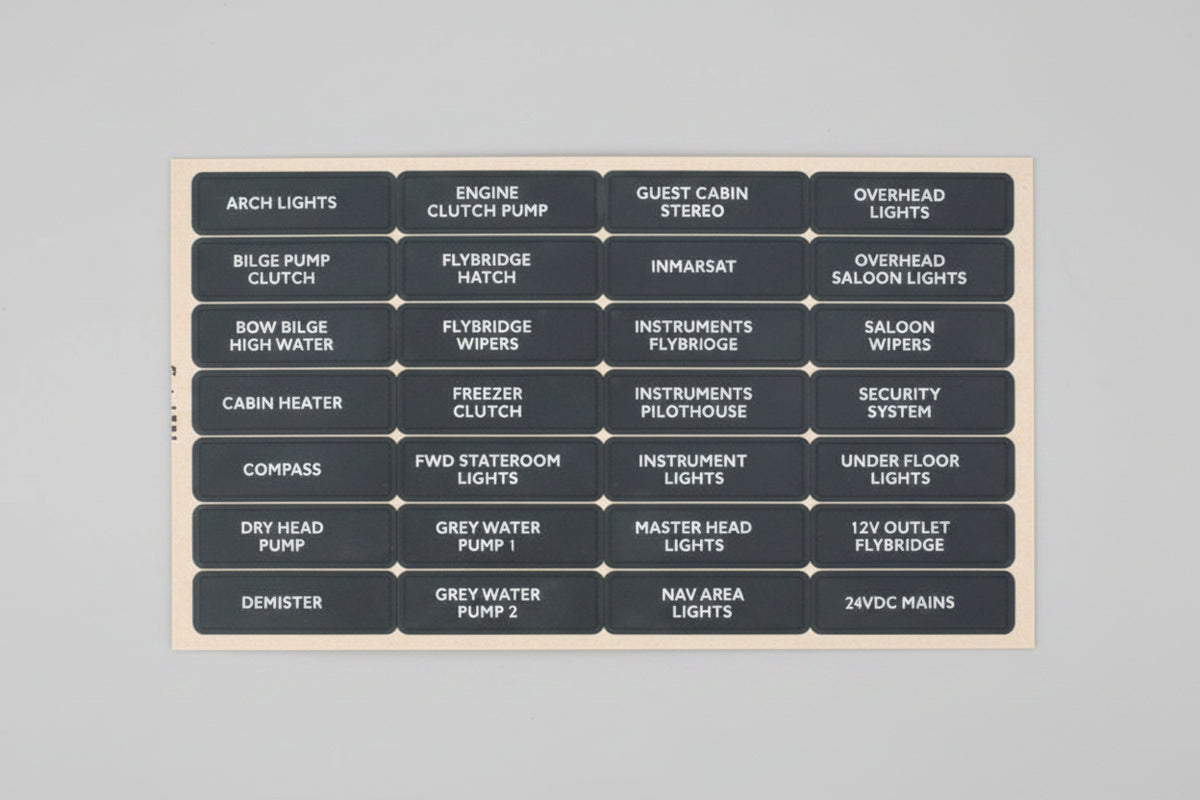 A dark gray rectangular panel with multiple small white labels arranged in a grid, showing automotive component names such as arch lights, engine clutch plate, fuse holder, cabin heater, compressor, and master head light.