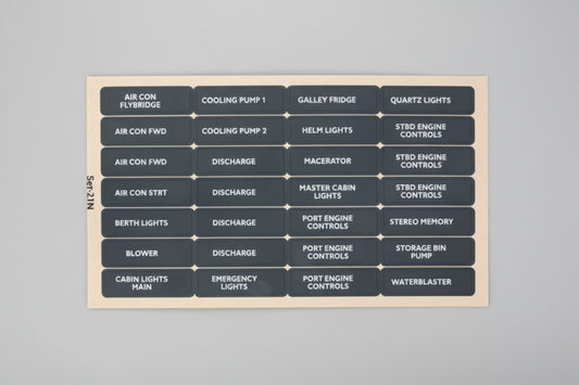 A dark gray rectangular panel filled with small light-blue and white rectangular labels arranged in a grid, showing automotive or technical system names such as air con, cooling pump, galley fridge, quartz lights, master cabin, engine controls, and waterheater.