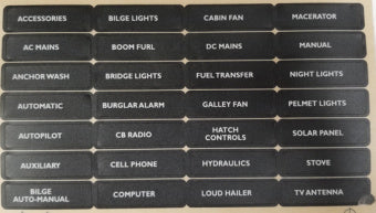 A grid of black rectangular labels with white printed text, showing various electrical and mechanical system names such as accessories, bilge lights, cabin fan, mains, manual, anchor wash, bridge lights, fuel transfer, night lights, burglar alarm, gallery fan, pelmel lights, autopilot, cr radio, match controls, solar panel, auxiliary, cell phone, hydraulics, stove, bilge auto-manual, computer, loud hailer, and tv antenna.